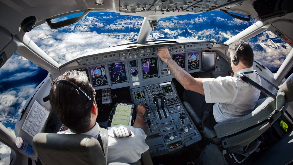 two pilots in an airplane cockpit, with a blue sky and clouds visible through windshield